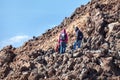Three hikers descend along a stone path among the lava piles high in the mountains in sunny and clear weather. The Teide Volcano,