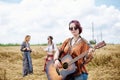 Three hippie women, wearing boho style clothes, dancing in the wheat field, playing guitar, laughing, Female friends, traveling