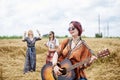 Three hippie women, wearing boho style clothes, dancing in the wheat field, playing guitar, laughing, Female friends, traveling