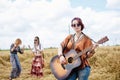 Three hippie women, wearing boho style clothes, dancing in the wheat field, playing guitar, laughing, Female friends, traveling