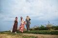 Three hippie women, wearing boho style clothes, walking on dirt road on green field, having fun. Female friends, traveling