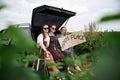 Three hippie women, wearing colorful boho style clothes, sitting on car trunk, holding Happy place sign, smiling, relaxing.