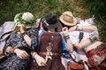 Three hippie women, wearing colorful boho style clothes and straw hats, lying, relaxing on green grass of field on sunny summer Royalty Free Stock Photo