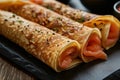 Three homemade thin pancakes stuffed with salmon, close up black plate, rustic style on wooden background Royalty Free Stock Photo