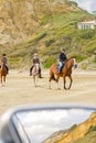 Three horses and riders on beach with dunes reflected in car rear vision mirror