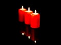 Three hot red candles arranged diagonally are reflected against the background of a black mirror. Royalty Free Stock Photo