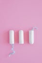 Three hygienic tampons on a pink background.