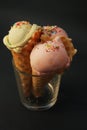 Three ice cream in waffle cone with scoop of pink fruit ice cream and confetti in glass isolated on dark blue background Royalty Free Stock Photo
