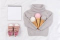 Three ice cream from yarn in waffle cones on gray knitted sweater, pink sneakers and open notepad on white background. Top view Royalty Free Stock Photo