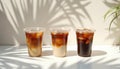 Three iced coffee drinks in plastic cups on white surface. Palm leaf shadows create summer mood. Refreshing cold beverage with Royalty Free Stock Photo