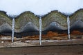 Three icicles on a slate roof under the snow against a brown wall