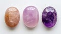 Three identical-sized gemstones, Amethyst, Rose Quartz, and Moonstone, aligned side by side, each displaying their