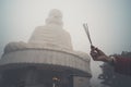 Three incense sticks in a woman's hand against a big Buddha in the fog. Bana hill. Vietnam. Danang. Buddha image with incense Royalty Free Stock Photo