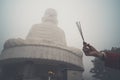 Three incense sticks in a woman`s hand against a big Buddha in the fog. Bana hill. Vietnam. Danang. Buddha image with incense Royalty Free Stock Photo