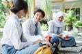 three Indonesian high school students smile while studying in groups sitting on the floor