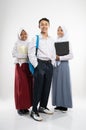 Three Indonesian teenagers wearing school uniforms smile at the camera with a backpack, a book, and a laptop computer