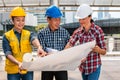 Three industrial engineer wear safety helmet engineering working and talking with drawings inspection on building outside.