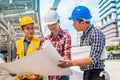 Three industrial engineer wear safety helmet engineering working and talking with drawings inspection on building outside