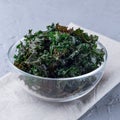 Three ingredient baked green kale chips with sea salt and olive oil, in glass bowl, square format