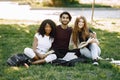 Three international students sitting on a grass in a park and holding a books Royalty Free Stock Photo