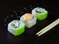 Three Japanese rolls at an angle, light chopsticks and sprinkled sesame seeds