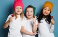 Three joyful friends kids in white t-shirts and colorful hats hold sweet lollipop candies happy smiling hugging