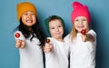 Three joyful friends kids in white t-shirts and colorful hats hold sweet lollipop candies happy smiling hugging