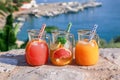 Three jugs with fresh drinks of grapefruit and orange juices, detox citrus water on a background of a seascape.