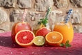 Three jugs with fresh drinks of grapefruit and orange juices, detox citrus water on an iron pink table.