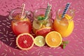 Three jugs with fresh drinks of grapefruit and orange juices, detox citrus water on an iron pink table.