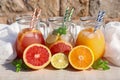 Three jugs with fresh drinks of grapefruit and orange juices, detox citrus water on a light wooden background.