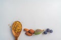Three juniper blue old berries, almonds nut and bee pollen in wooden spoon on spring, isolated on white textured paper. Copy space Royalty Free Stock Photo