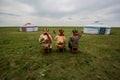 Three Kalmyk musicians in national costumes in the steppe against the background of yurts, the spring steppe