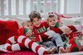 Three kids in Christmas pyjamas laying on white big bed with Christmas pillows