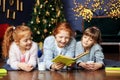 Three kids girls are reading a book on Christmas Eve. The concept of Merry Christmas, New Year, family and gifts Royalty Free Stock Photo