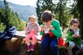 Three kids resting in mountains and drink juice from stick pack sachet. Travel and hiking with childrens