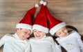 Three kids in Santa hats lying on wooden background, having fun and happy emotions, winter holiday concept Royalty Free Stock Photo