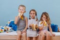 Three kids in sleeping clothes sitting on unmade bed, eating bananas Royalty Free Stock Photo