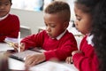 Three kindergarten school kids sitting at desk in a classroom using a tablet computer and stylus together, selective focus Royalty Free Stock Photo