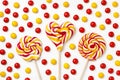 Three large lollipops on a stick in the shape of a circle, a flower and a heart surrounded by red and yellow candies on a white