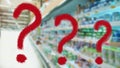 Three large red question mark on abstract blur image of supermarket background. Defocused shelves with products. Grocery shopping