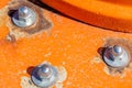 Three large, round, unpainted screws are screwed into metal on orange structure