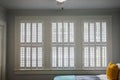 Three large windows with cream colored plantation shutters that are closed on the interior of a cottage style house Royalty Free Stock Photo