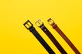 Three leather belt for trousers on yellow background. Top view flat lay