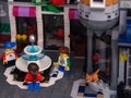 Three Lego child minifigures standing around a fountain in the city square. A ginger cat seating on bakery porch