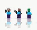 Three lego minecraft mini figures with toy guns attacking. Isolated on white background with reflective shadow