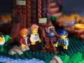 Three Lego minifigures standing under a tree and cooking food on a campfire