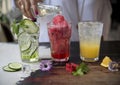 Three lemonades. Cucumber, watermelon and orange on rustic background. In the background the hand of a girl pouring mineral water