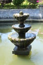 Three-level fountain in an ornamental pond. Weak streams of water spill over the edges of the fountain floors. Green algae create