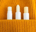 Three lip balms on the orange knitted background pocket. Winter lip care sticks with beeswax, honey, panthenol and shea butter.